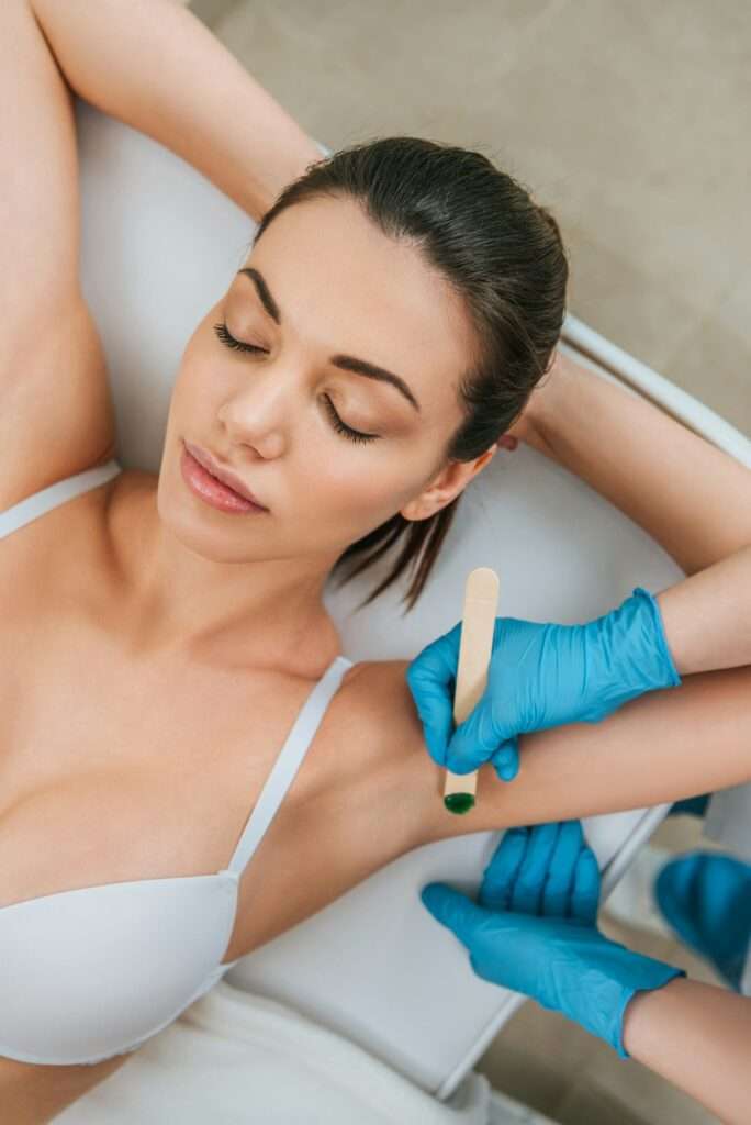 Cropped view of cosmetologist using putty knife for armpit wax depilation