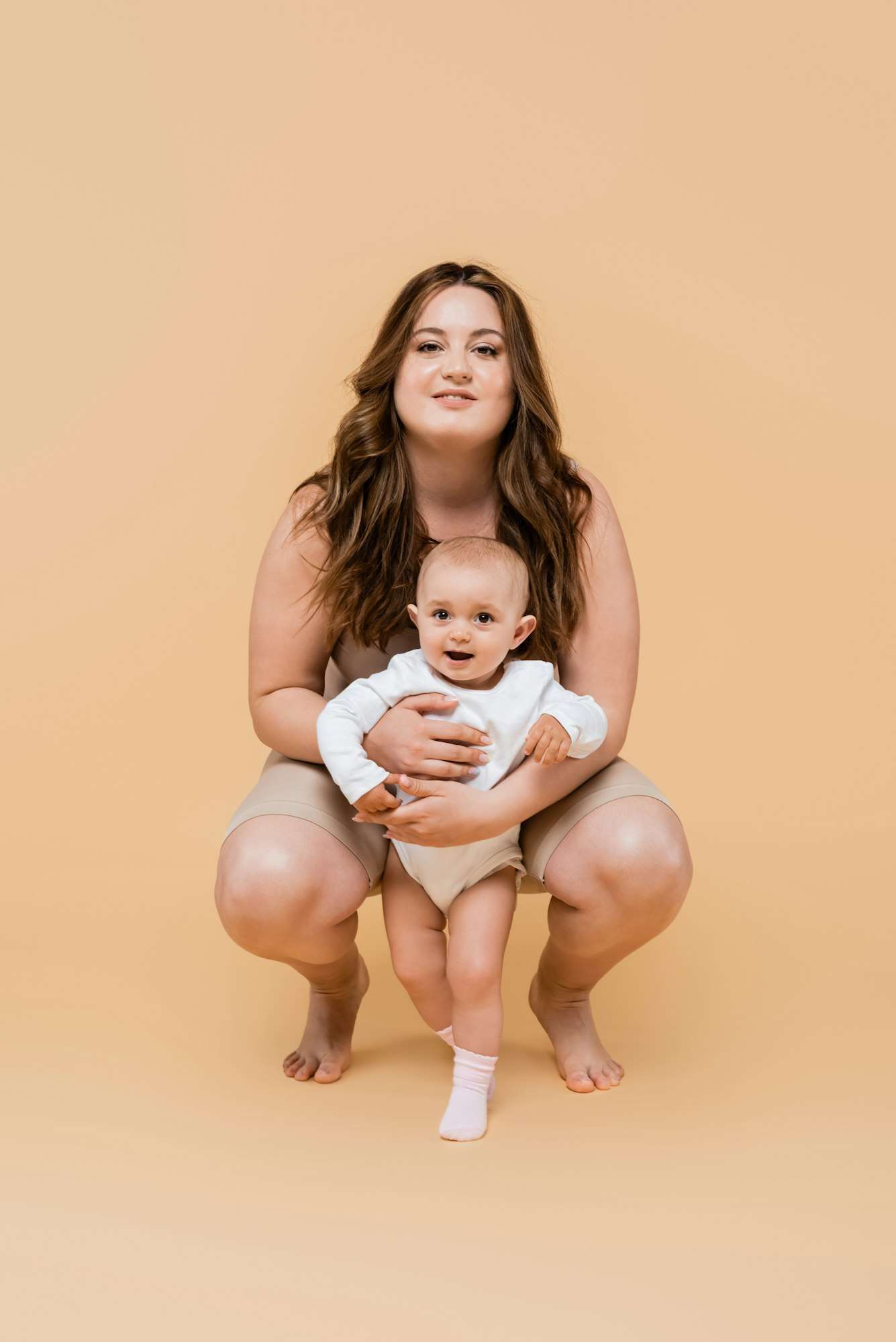 Happy plus size mom hugging baby daughter on beige background