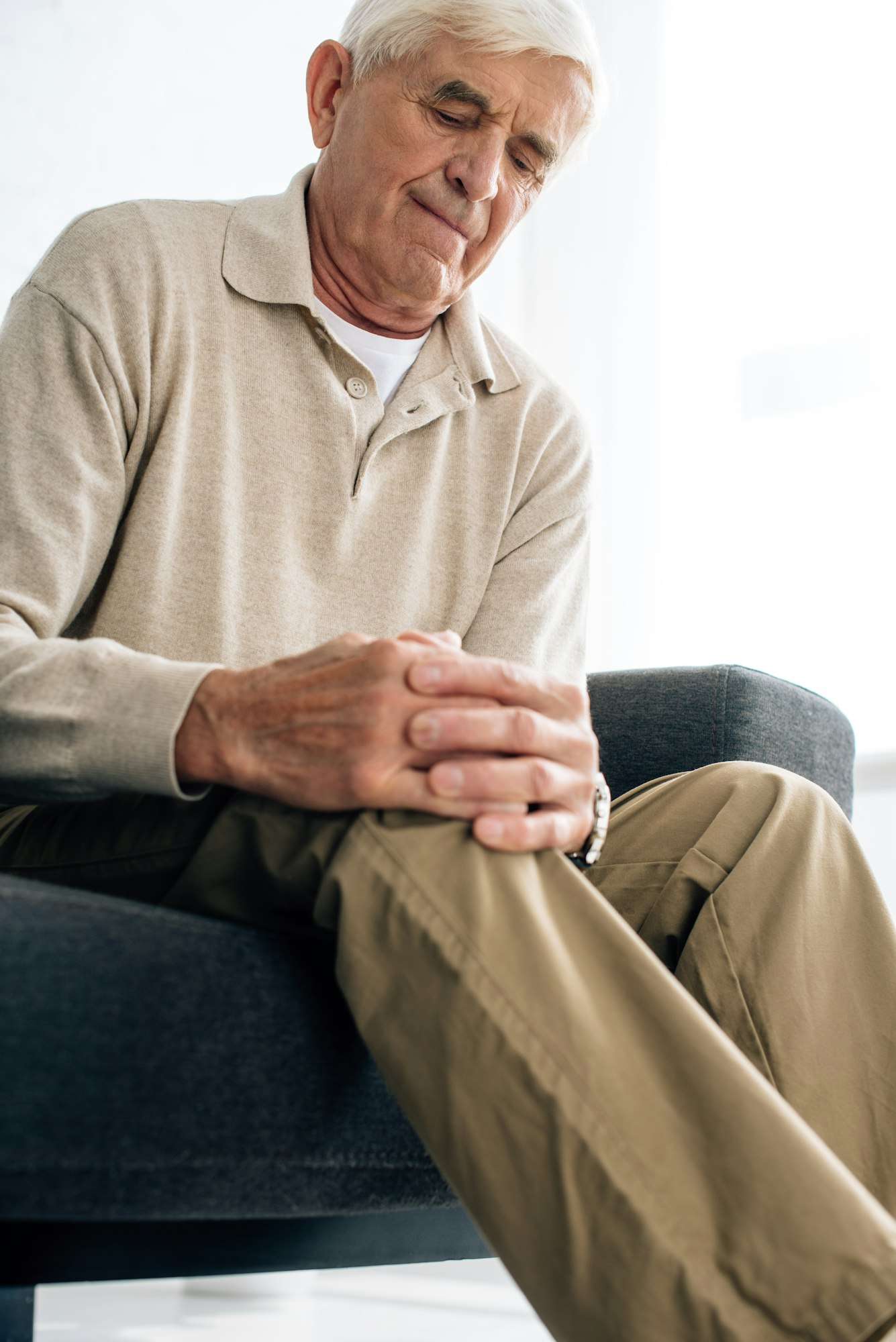 low angle view of senior man sitting on sofa and having knee Arthritis in apartment