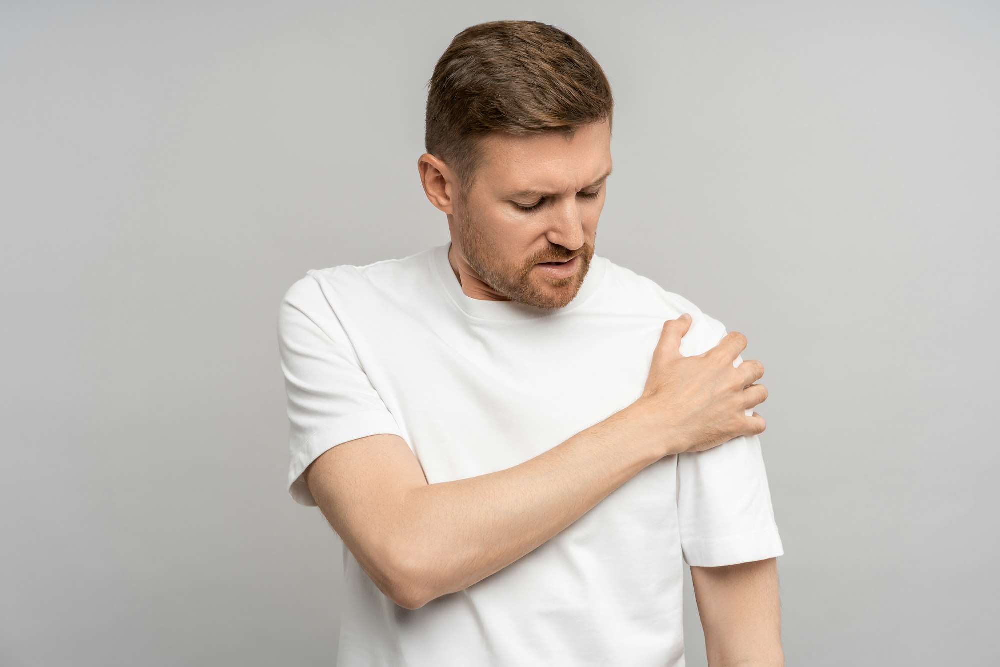 Unhealthy man holds on to sore shoulder. Guy experiences throb pain in ligaments, suffers discomfort